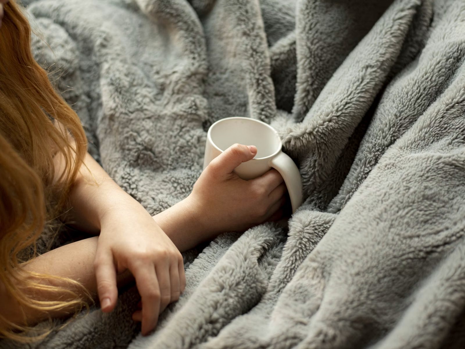 Frau in eine Decke gehüllt mit einer Tasse – ständiges Frieren als Anzeichen einer Schilddrüsenunterfunktion
